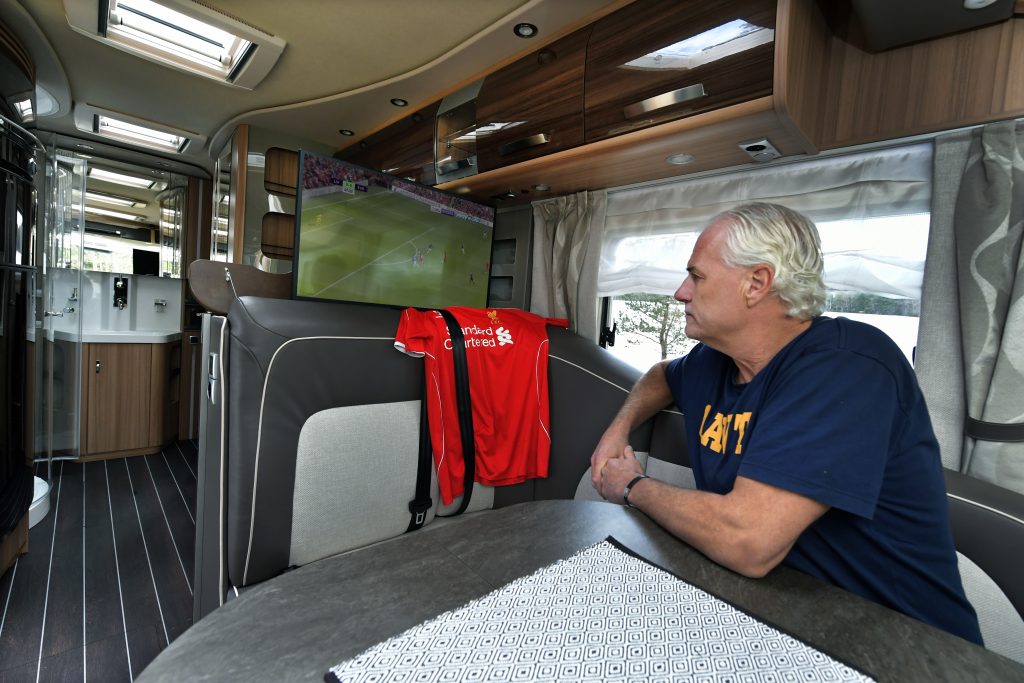 Glenn Hysén sitter i husbil och tittar på tv:n där fotboll visas